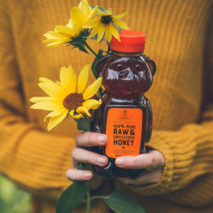 Hands holding a bear-shaped bottle of Nate's honey and a sunflower against a sweater.