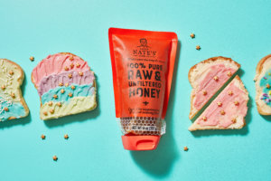 A pouch of Nate’s raw & unfiltered honey next to pieces of toast with colorful spreads on a blue background.