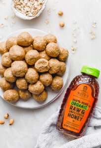 A white plate full of peanut butter cookie bites beside a bottle of Nate's 100% pure organic raw & unfiltered honey. 