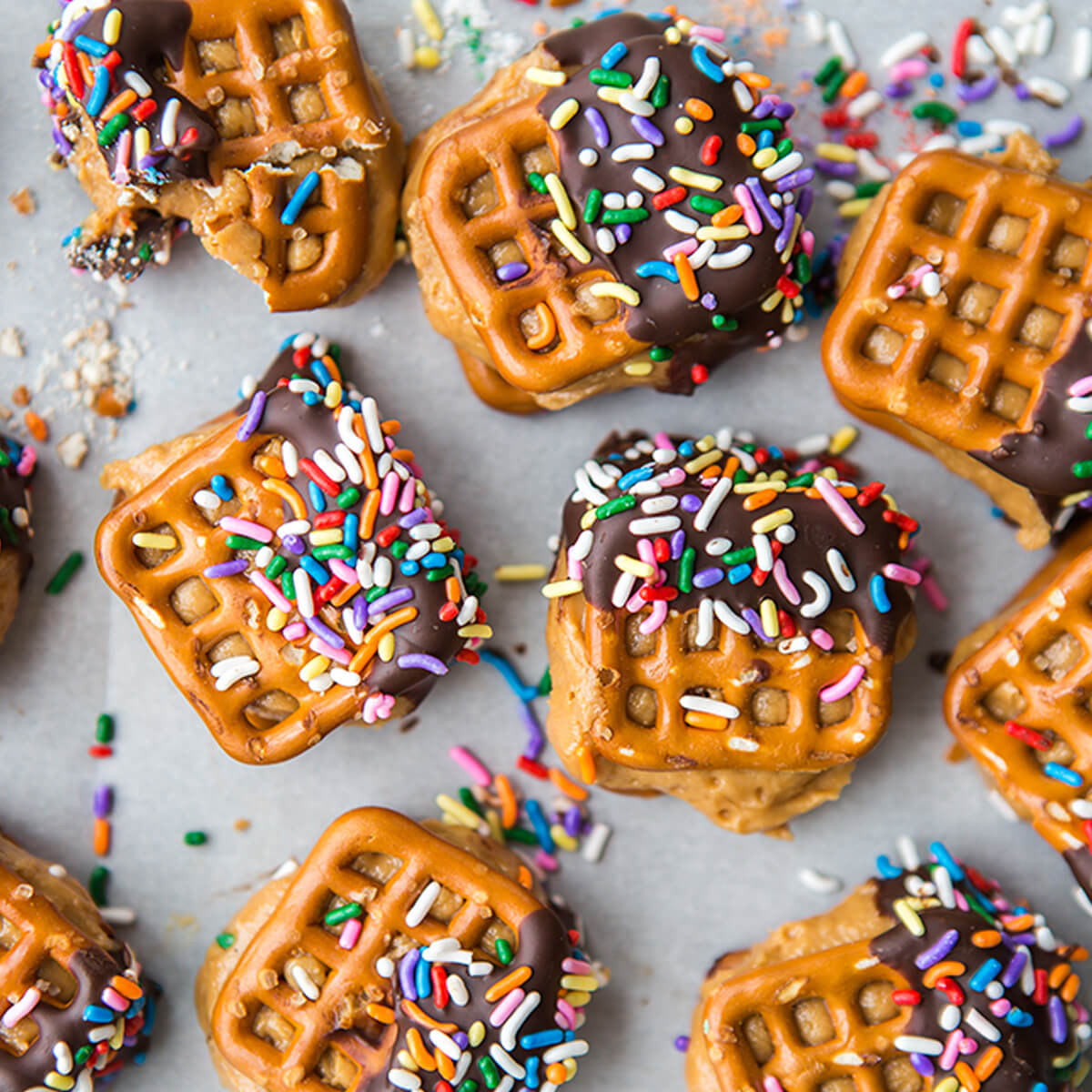 Pretzels filled with peanut butter and honey and dipped in chocolate and colorful sprinkles on parchment paper.